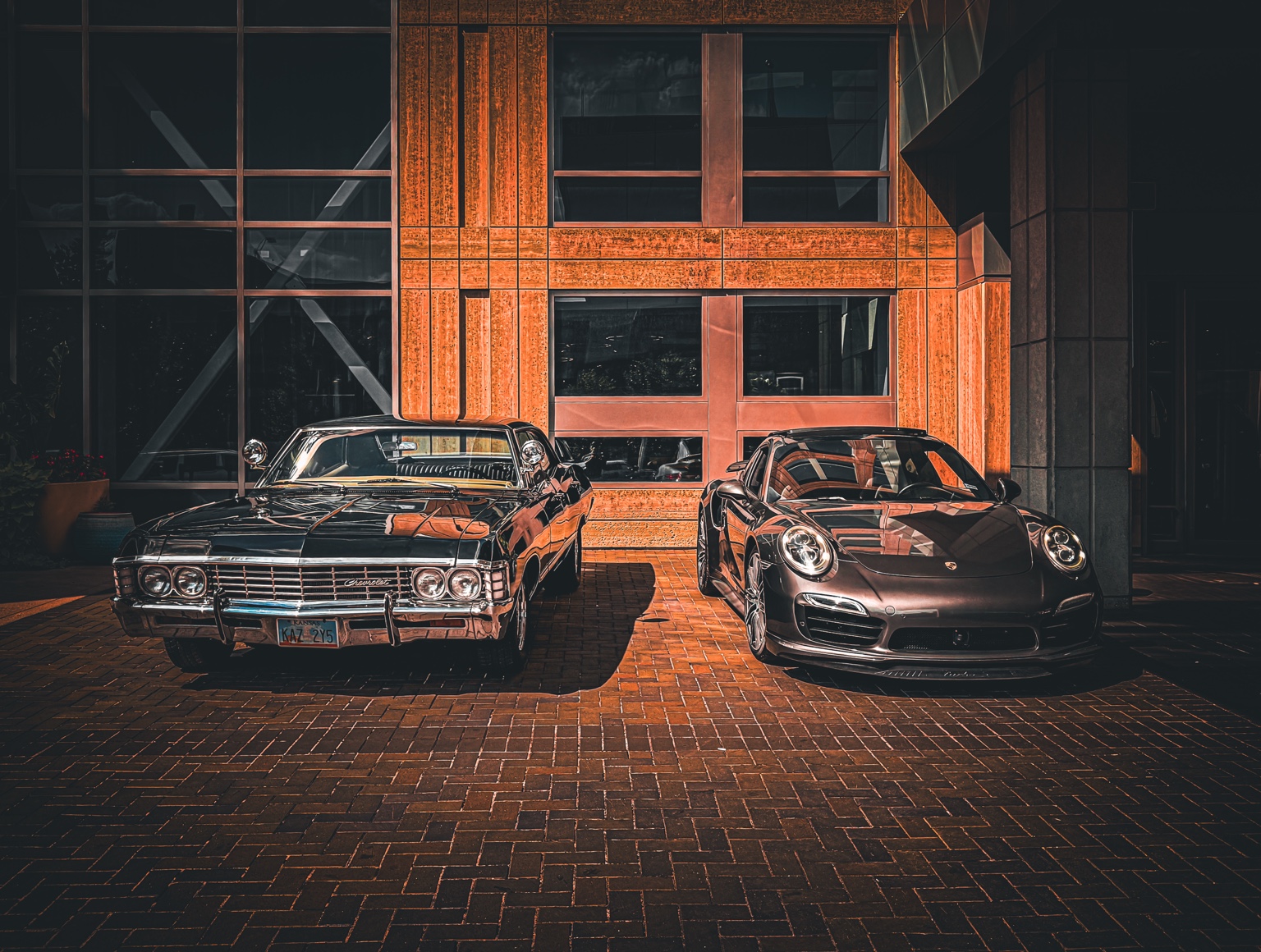 Classic Chevrolet and modern Porsche parked beneath warm architectural panels