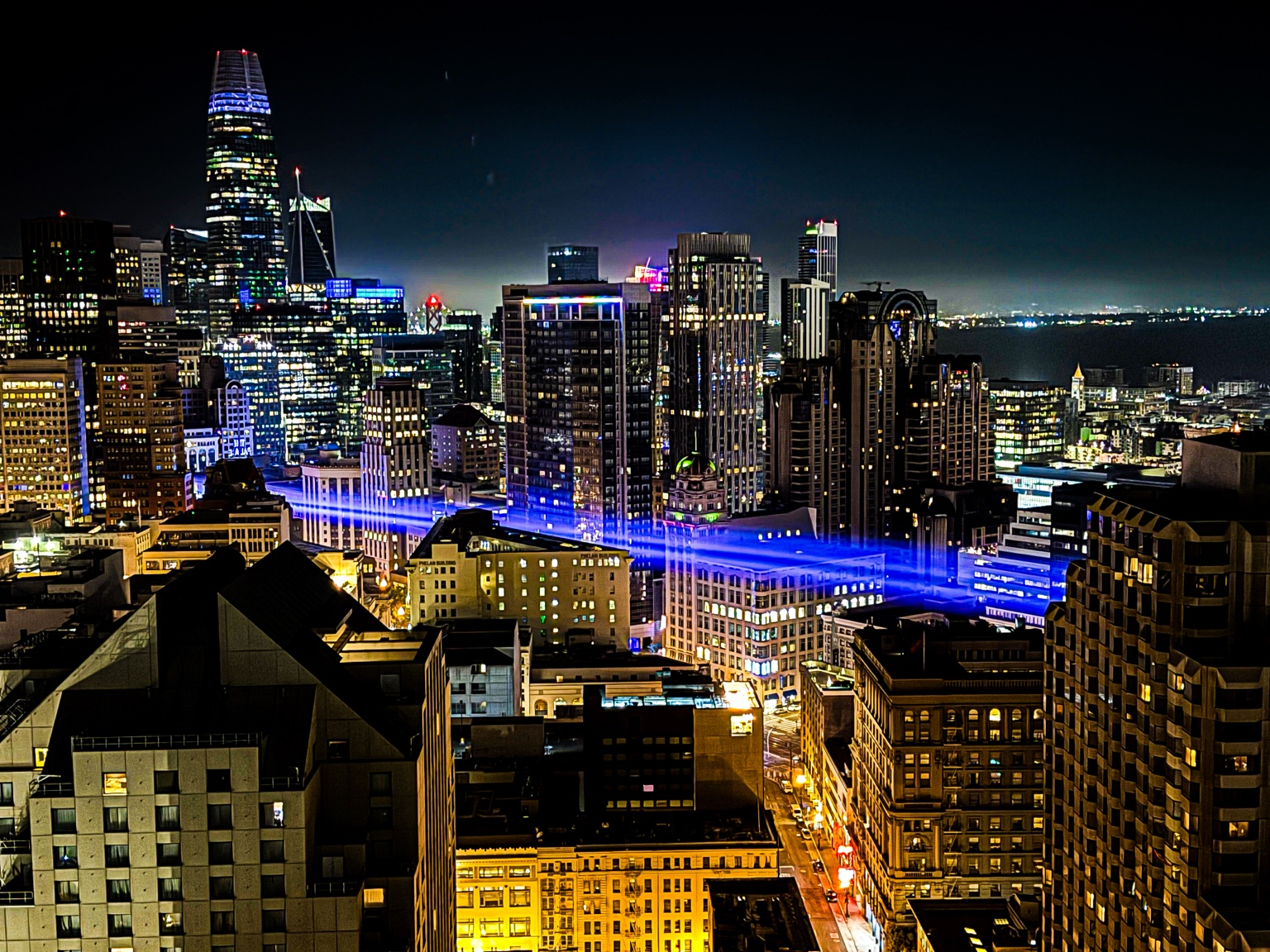 Illuminated high-rise buildings and a blue-lit rooftop beneath a dark sky