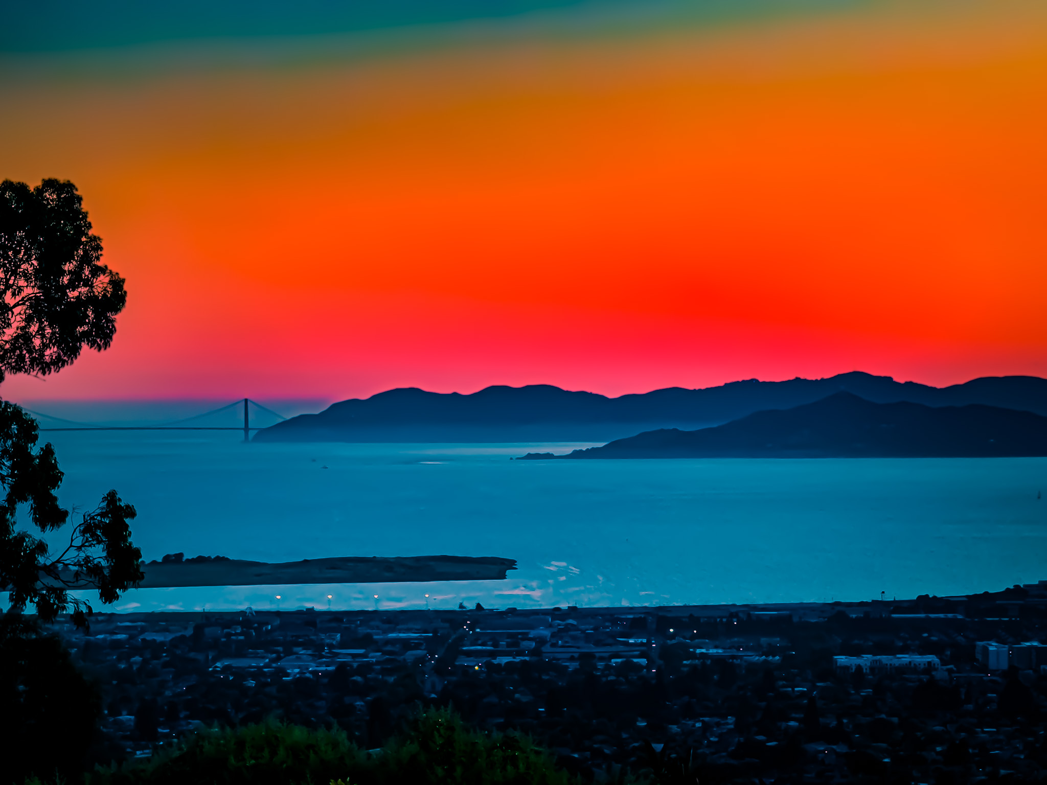 Orange and red sunset above layered hills and blue bay water