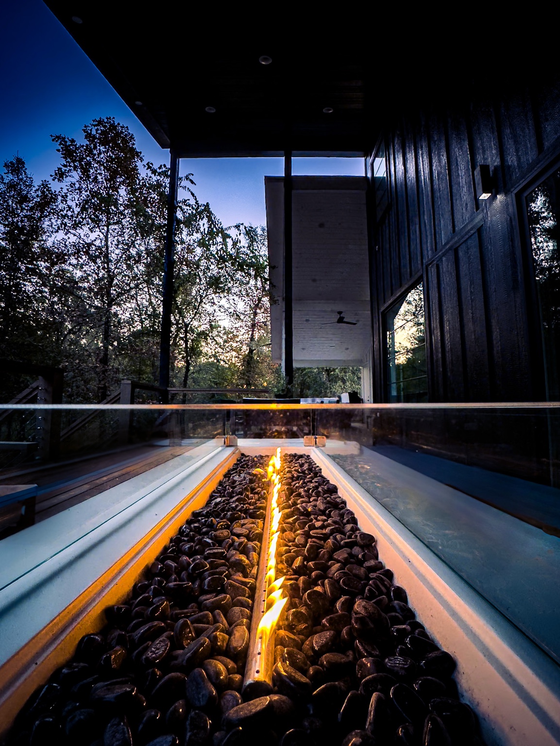 Linear fire feature leading toward glass doors and trees at dusk