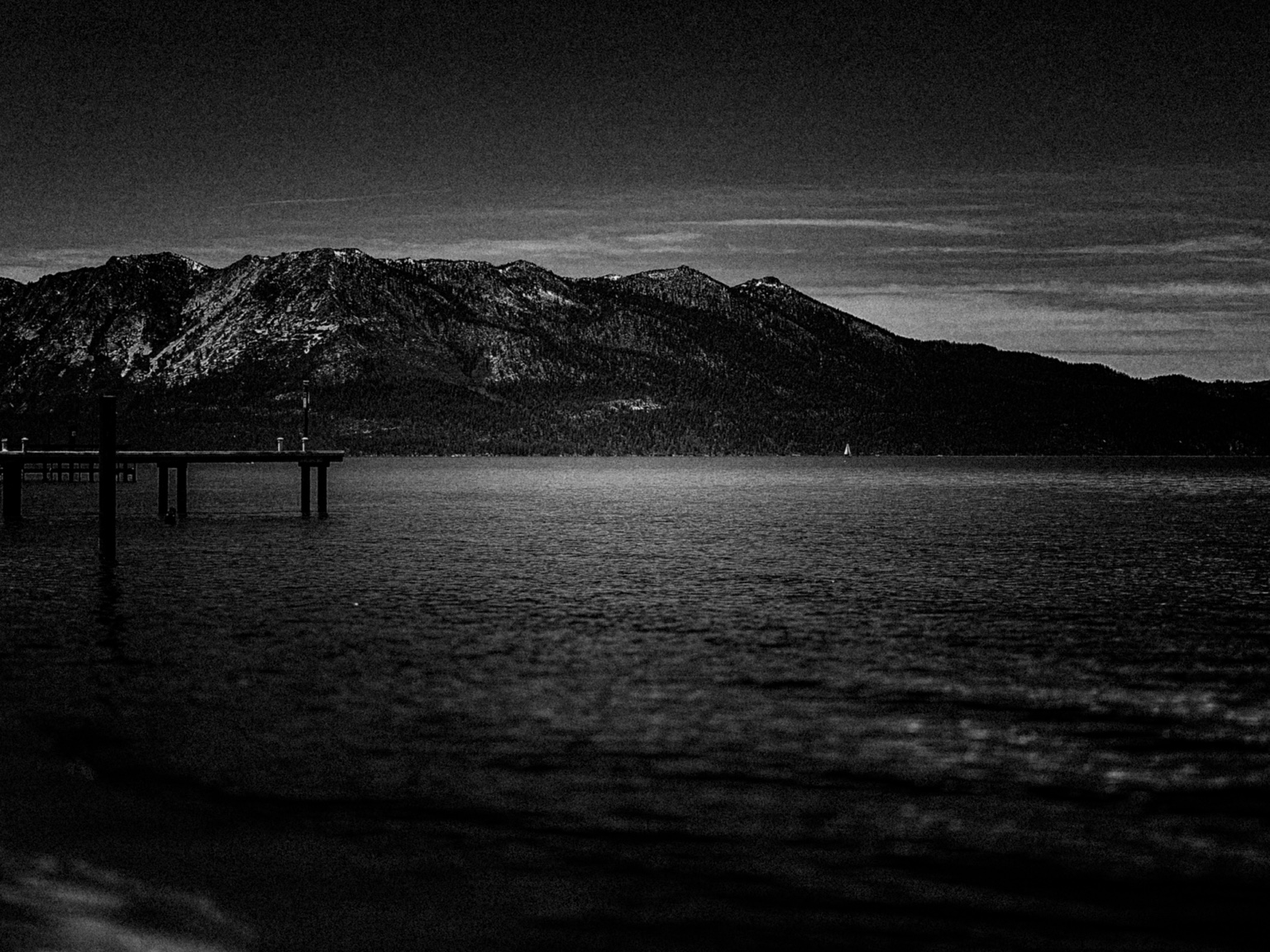 Black-and-white lake beneath a textured sky and a rugged mountain ridge