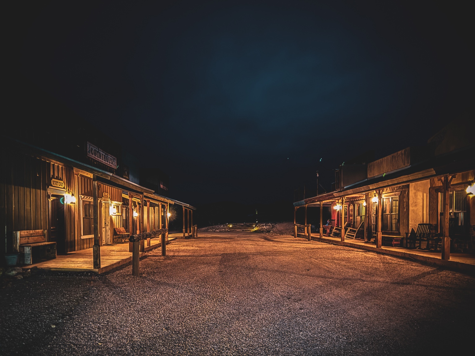 Quiet western-style storefronts lit by warm lamps beneath a dark evening sky